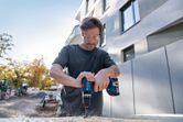 安全装置を装着した人がコードレスドリルを使用して屋外で木材に穴を開けています。