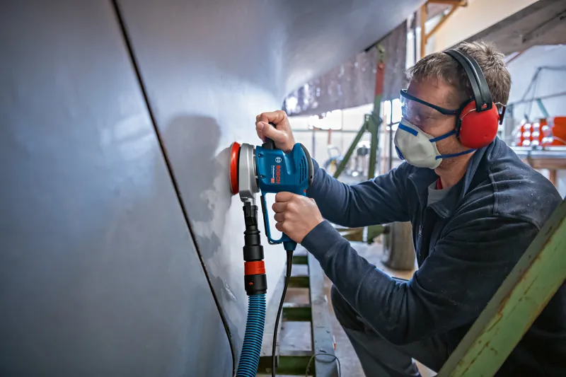 安全装置を装着した人がランダムオービットサンダーで広い表面を研磨しています。.
