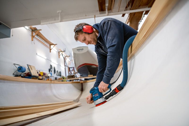 安全装備を身に着けた人が木製の船体の内部を研磨しています。.