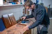 安全装備をつけた人がランダムオービットサンダーで木の板を研磨しています。