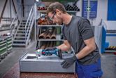 安全装置を装着した人がコードレスニブラーで金属板をトリミングしています。
