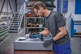 安全装置を装着した人がコードレスニブラーで金属板をトリミングしています。.