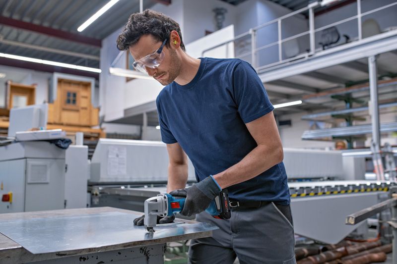 安全装置を装着した人がコードレス金属鋏で金属板を切断します。.