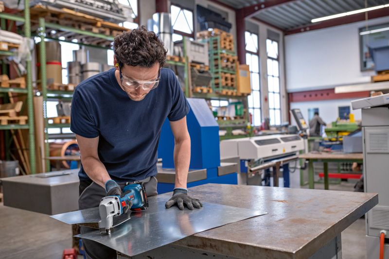 安全装置を装着した人がコードレス金属鋏で金属板を切断します。.