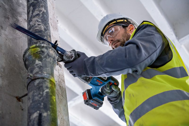 安全装置を装着した人がレシプロソーでパイプを切断しています。.