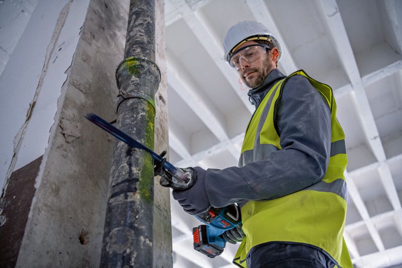 安全装置を装着した人がレシプロソーで金属パイプを切断しています。.