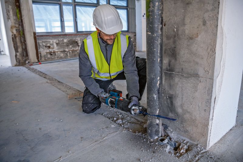 安全装置を装着した人がレシプロソーを使用して金属パイプを切断しています。.