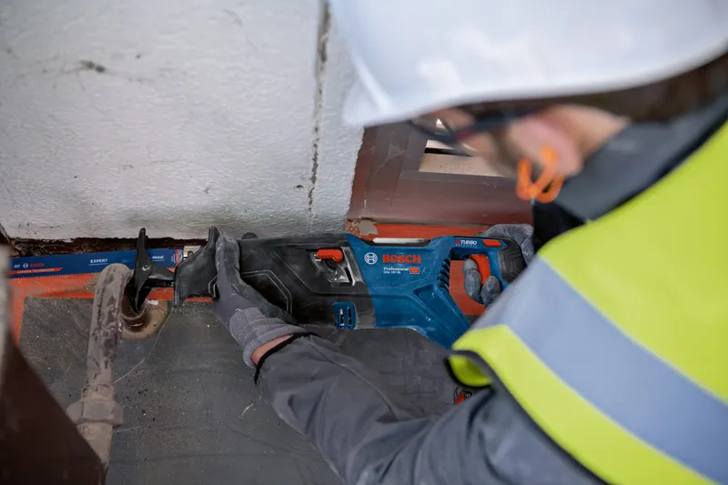 安全装置を装着した人がレシプロソーを使用して金属パイプを切断しています。.