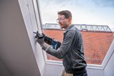 安全装置を装着した人がレシプロソーで壁を切っています。.