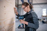 安全装備を身に着けた人が作業場で木の板に穴を開けています。