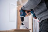 コードレス電動ドリルで木材に穴を開ける人。.