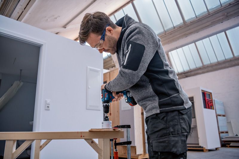 安全装置を装着した人がコードレス電動ドリルを使用して木材に穴を開けています。.