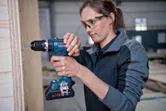 安全装置を装着した人が木製パネル上でコードレスドリルを使用しています。