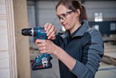 安全装置を装着した人が木製パネル上でコードレスドリルを使用しています。.