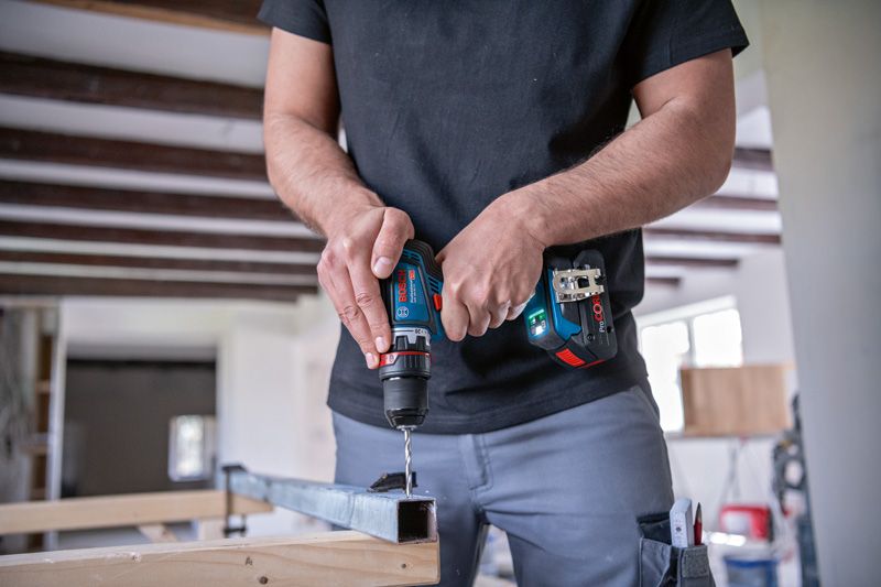 作業場内でコードレスドライバーを使用して金属の梁に穴を開ける作業者。.