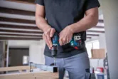 作業場内でコードレスドライバーを使用して金属の梁に穴を開ける作業者。