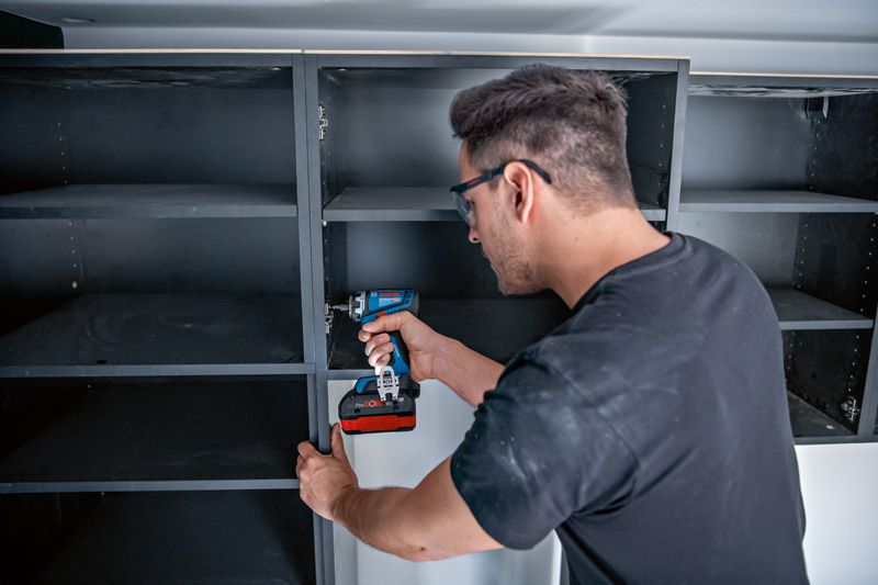 安全装置を装着した人がコードレスドリルまたはドライバーを使用して棚を組み立てます。.