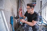 安全装備を身に着けた人が、集塵機を使ってコンクリートの壁に穴を開けています。.