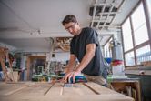 安全装備を身に着けた人がコードレスオービタルサンダーで木製のドアを研磨しています。