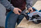 木製の作業台の上で、丸鋸に集塵ホースを接続している人。.