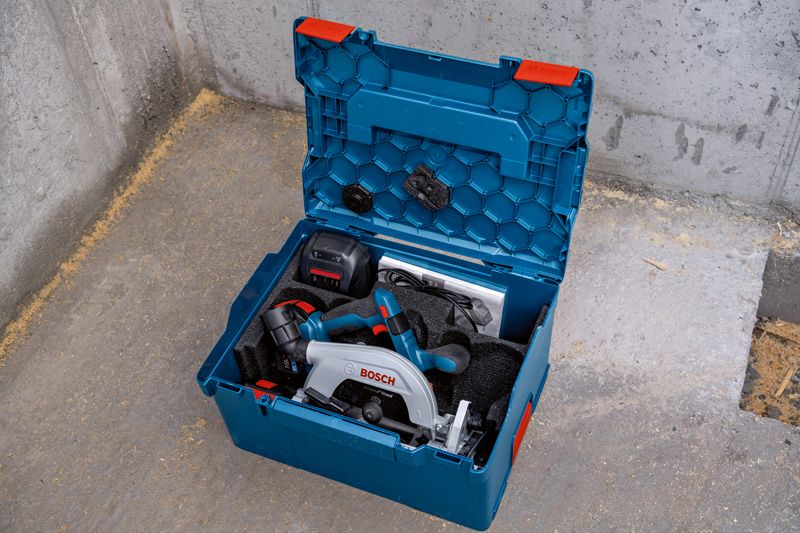 コンクリートの床の上に置かれた青いキャリングケースに入ったコンパクトな丸鋸キット。.