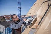安全装備を身に着けた人が丸鋸で傾斜した屋根の上の木の板を切っています。