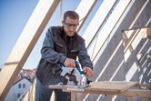 安全装置を装着した人が建設現場で丸鋸を使用して合板を切断しています。