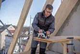 建設現場で安全装備を身に着けた人が丸鋸で木材を切っています。.
