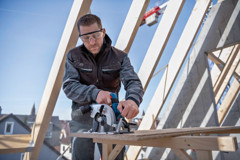 建設現場で安全装備を身に着けた人が丸鋸で合板を切っています。.