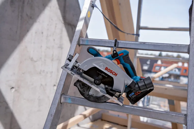 建設現場の金属製のはしごの上に置かれたコードレス丸鋸。.