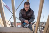 安全装備を身に着けた人が建設現場で電動のこぎりを使って木材を切断しています。