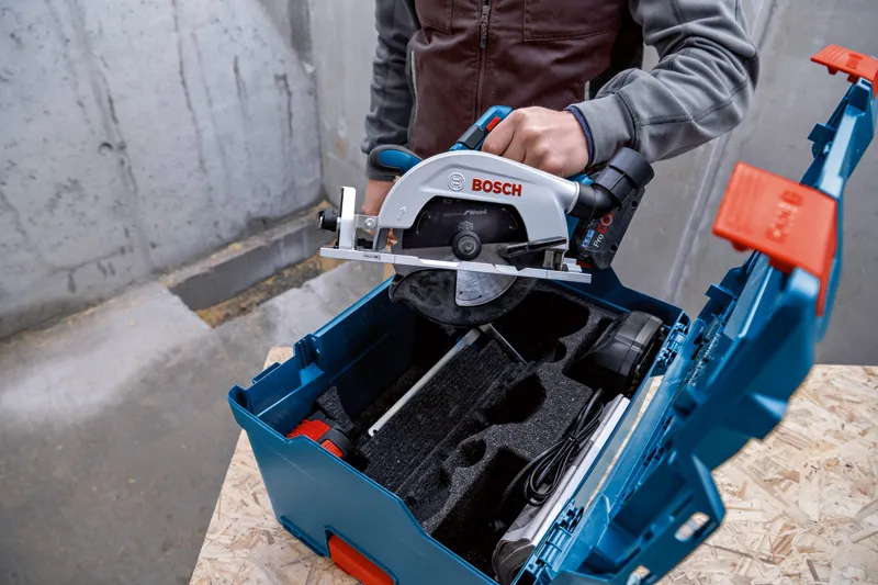 人が丸鋸を木製の表面にある青い工具ケースに入れています。.