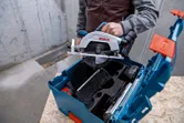 人が丸鋸を木製の表面にある青い工具ケースに入れています。