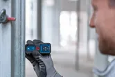 安全装置を装着した人がレーザー測定器を使用して金属梁上の距離をチェックしています。