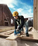 安全装備を身に着けた人が建設現場でジグソーを使って木材を切っています。