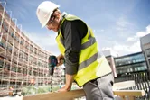 安全装備を身に着けた人が建設現場で木材に穴を開けています。