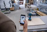 木工所で、スマートフォンを使ってコードレスドリルを参照している人。