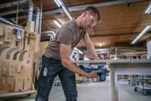 安全装備を身に着けた人が作業場で電動のこぎりで木の板を切っています。