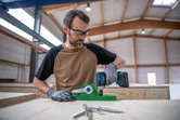 安全装置を装着した人が木製の作業台の上でコードレスドリルを使用しています。