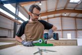安全装置を装着した人が木製の作業台の上でコードレスドリルを使用しています。.