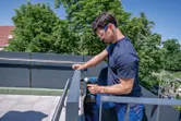 安全装備を身に着けた人が電動ドリルで金属製の手すりのネジを締めています。