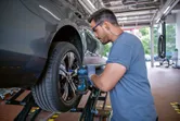 安全装備を身に着けた人がインパクトレンチを使って車のホイールのボルトを締めています。