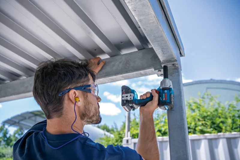 安全装置を装着した人が金属構造物に対してインパクトレンチを使用しています。.