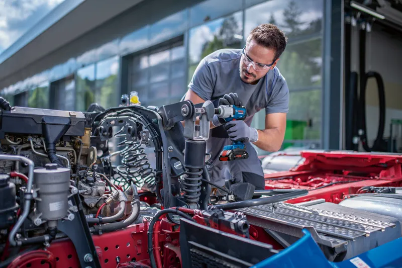安全装備を身に着けた人が、車両シャーシ上でコードレスインパクトレンチを使用しています。.