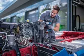 安全装備を身に着けた人が、車両シャーシ上でコードレスインパクトレンチを使用しています。.