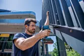 安全装置を装着した人が金属製のフェンスにコードレスインパクトレンチを使用しています。.