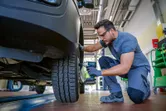 安全装備を身に着けた人が、コードレスインパクトレンチを使用して自動車のホイールボルトを締めています。.
