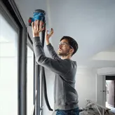 安全装備を身に着けた人が電動サンダーで窓の近くの天井を研磨しています。