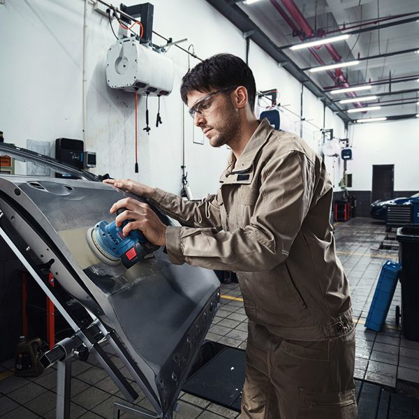安全装備を身に着けた人が電動サンダーで車のドアを研磨しています。.