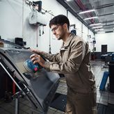 安全装備を身に着けた人が電動サンダーで車のドアを研磨しています。.